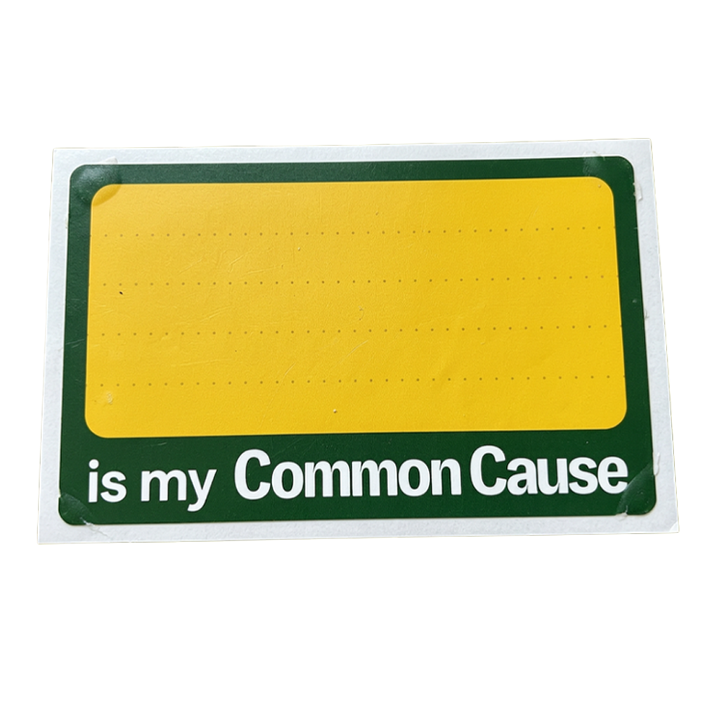 A rectangular sign with a yellow center panel bordered by dark green, with the phrase 'is my Common Cause' in white text along the bottom, photographed on a plain white background.