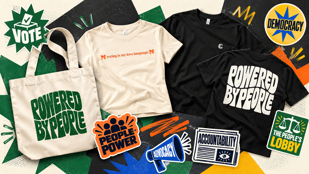 A flat-lay product display featuring three t-shirts and a canvas tote bag with various political advocacy graphics and stickers, including slogans like 'POWERED BY PEOPLE' and 'VOTING IS MY ABOLISH BILINGUALITY' on a colorful patterned background.